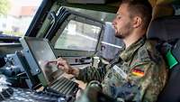 Ein Soldat sitzt in einem Fahrzeug vor einem Laptop in einer olivfarbenen Metallhülle.