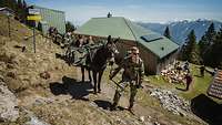 Soldaten stehen mit Mulis, die militärische Ausrüstung tragen, auf einem Pfad an einem Berghang