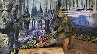 Eine Ausstellungspuppe in Uniform sitzt auf einem Baumstamm vor einem Foto mit Soldaten im Wald.