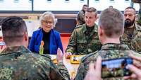 A female civilian and many soldiers are sitting at a table in a well-lit dining facility.