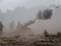 Soldiers stand in dense smoke, firing a field howitzer from which a projectile is expelled with more smoke.