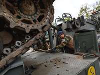 A tank sits on a heavy equipment transporter, a soldier loosens the lashing.