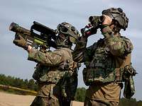 One soldier shoulders a surface-to-air-missile while another looks through his binoculars.