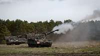 Three firing self-propelled howitzers on a field