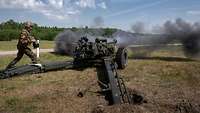A light field howitzer during firing. A soldier tugs on the pull cord to fire.