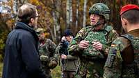 A reporter in a black parka is standing in front of a soldier, wearing helmet and protective vest, asking him questions.