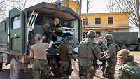 The open rear of an ambulance. A wounded person on a stretcher is being lifted out of the vehicle by soldiers.