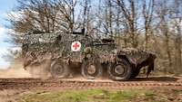 An armoured medical vehicle is driving by quickly on a forest path.