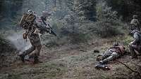 A wounded soldier is lying on a forest path. His fellow soldiers are rushing to his assistance.