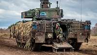 An infantry fighting vehicle is standing on a forest path. A soldier is shouting out of the open rear ramp.