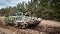 An IFV drives at full speed along a sandy track at the edge of a forest.