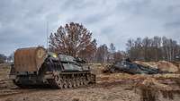 Two armoured vehicles with huge shovels dig a pit on a plain.