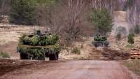 Several main battle tanks move in single file along a track on an open area, keeping a large gap between them.