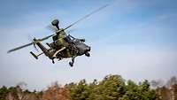 An attack helicopter flies fast over a forest.