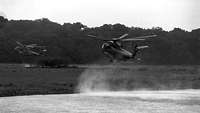 Two CH-53 helicopters in low-level flight above a stretch of water.