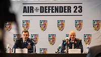 An American general and a German general sitting behind microphones.