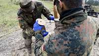 Zwei Soldaten mit blauen Handschuhen wickeln eine Schnur um einen Baum auf einer Freifläche.