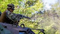 Ein Soldat schaut aus einem Panzer und schießt mit einem Maschinengewehr.