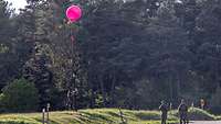 Mehrere Soldaten lassen auf einer Lichtung einen roten Ballon steigen.