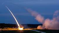 Zwei Raketenwerfer feuern nachts auf einem Feld Raketen ab und erzeugen Rauch und helles Feuer.