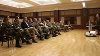 Soldaten sitzen in einem Saal. Vor ihnen steht ein Soldat an einem Rednerpult und spricht. 