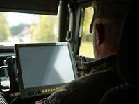 Auf dem Beifahrersitz in einem Fahrzeug sitzt ein Soldat vor einem Bildschirm.