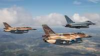 Three differently painted fighter jets are seen during a flight over green landscape