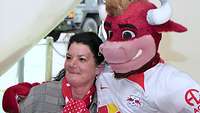 Eine Frau steht neben dem Maskottchen des RB Leipzig und schaut zur Kamera.