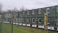 You can see green containers lined up in a row behind a fence.