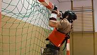 Ein Soldat in Schutzrüstung und Uniform macht in einer Sporthalle Klimmzüge am Torpfosten.