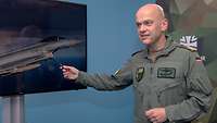 Ein Soldat in Fliegeruniform zeigt während eines Interviews mit einem Stift auf einen Monitor
