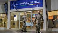 Zwei Soldaten tragen eine Kiste, hinter ihnen ein Gebäude mit der Aufschrift „MHQ EUTM MALI“.