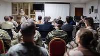 Eine Gruppe von Menschen sitzt in einem Vortragsraum. Am Pult im Hintergrund steht ein Soldat.