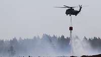 Ein Hubschrauber lässt über einem brennenden Moor Wasser ab.