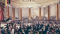 Farbillustration eines großen gefüllten Sitzungssaals; links ein Redner am Rednerpult.