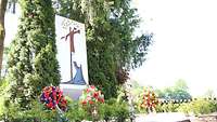 Ein Denkmal mit einem stilisierten Jesus am Kreuz und Mutter Maria, davor vier abgelegte Kränze