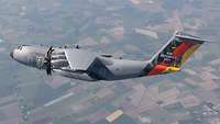 An A400M flies over German fields. The fin is foiled with German flag and the Brandenburg Gate.