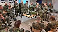 Soldaten sitzen um einen Tisch, an dem ein Soldat steht, der die Sanitätsausrüstung erklärt.