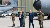 Auf einem Flughafen gehen mehrere Soldaten und Politiker vor einem Flugzeug