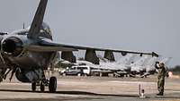 An American F-18 is standing on the tarmac. A soldier is standing next to it.