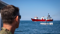 Ein Mann mit Sonnenbrille schaut auf See auf zwei Boote.