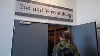 Besucher betreten einen Ausstellungsraum. Über der Tür steht „Tod und Verwundung“.