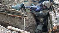 An einer Abzweigung eines Schützengrabens kniet sich ein Soldat in eine Deckung. Er ist mit einem Gewehr bewaffnet. 