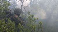 Ein Soldat kniet in einem Busch. Vor ihm ist viel Nebel, der die Sicht erschwert.