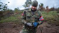 Ein Soldat steht im Gelände auf einem Truppenübungsplatz und hält die Reste einer Granate in der Hand