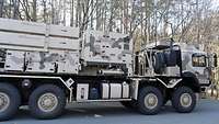 Ein vierachsiger Bundeswehr-Lkw mit Abschussvorrichtung zum Verschießen von Lenkflugkörpern vor einem Wald.