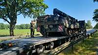 Zwei Soldaten stehen auf einem Schwerlasttransporter und hantieren an einem Bergepanzer Büffel