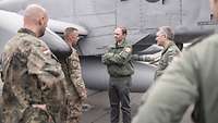 Four people are standing in front of a fighter jet and talking.