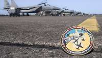 Frog perspective: A patch lies on the asphalt and fighter jets are in the background.