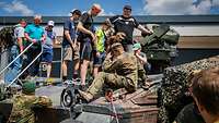 Besucher und Soldaten stehen auf einem Panzer am Tag der Bundeswehr